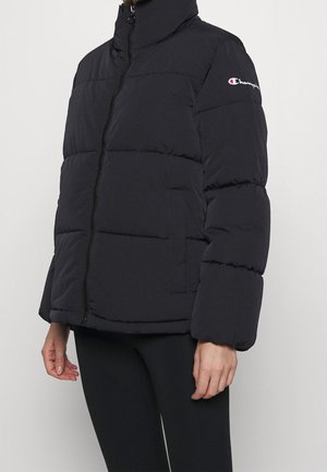 Czarna kurtka puchowa z przednim zamkiem błyskawicznym, wysokim kołnierzem, bocznymi kieszeniami i logo Champion na lewej górnej rękawie, noszona z czarnymi spodniami.