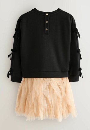 Schwarzes Sweatshirt mit Knopfdetails und seitlichen Bandakzenten, kombiniert mit einem pfirsichfarbenen, gerafften Tüllrock mit dezentem Glitzer.