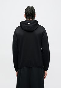 Μαύρο φούτερ με κουκούλα, κορδόνι και λογότυπο στο πίσω μέρος. Ομαλή υφή, μακρυά μανίκια και άνετη εφαρμογή.