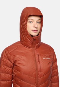 Rote isolierte Jacke mit Kapuze, mit glatter Textur, diagonalem Steppdesign und einer Reißverschlusstasche auf der Brust. Markenzeichen deutlich sichtbar.