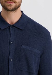 Marineblaue Hemd mit Kragen aus strukturiertem Strickstoff, mit einer Brusttasche und Knopfleiste.