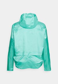 Giacca leggera con cappuccio di un brillante colore turchese. Presenta una texture liscia e lucida con un sottile motivo a reticolo e un design con retro corto.