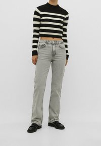 Suéter corto a rayas en blanco y negro combinado con jeans rectos grises y zapatos negros, con un diseño clásico y tejido texturizado.