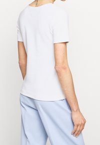 Top bianco a maniche corte con scollatura rotonda e orlo senza cuciture, abbinato a pantaloni azzurri chiari, che mostrano una texture liscia e aderente.