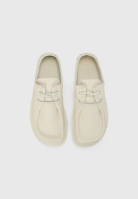 Cremefarvede læderslippers med rund tå, syede detaljer og et minimalistisk design. Har en glat overflade og subtile accenter.