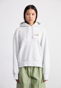 Light grey hoodie with a front kangaroo pocket, ribbed hem, and drawstring hood. Features small orange and red "Carhartt" logo on the chest.