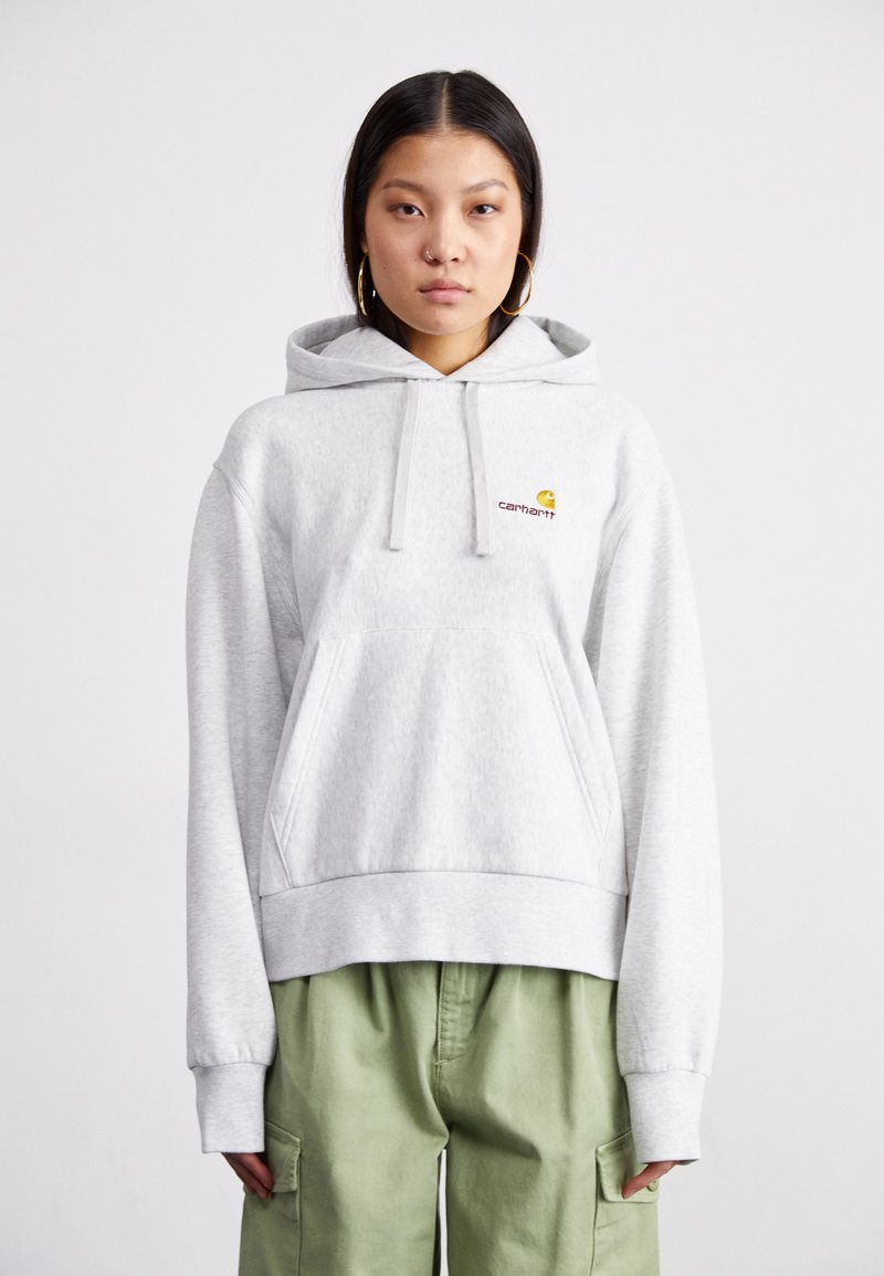 Light grey hoodie with a front kangaroo pocket, ribbed hem, and drawstring hood. Features small orange and red "Carhartt" logo on the chest.