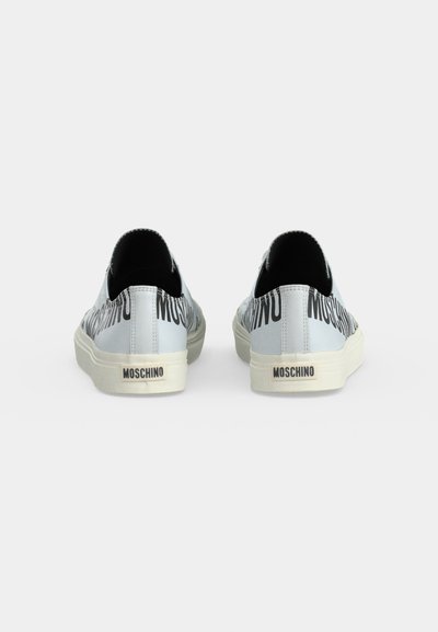 Paire de baskets slip-on blanches Moschino avec logo noir en gras et semelles beiges, vues de dos sur un fond clair.