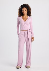 Light pink wrap top and loose-fitting pants made of a soft, smooth fabric; features a tie at the waist and long sleeves.
