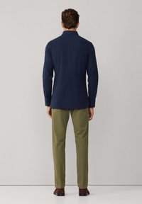 Camisa azul marino de manga larga con puños abotonados, que presenta un cuello clásico y un corte recto, combinada con pantalones verde oliva y zapatos marrones.