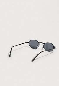 Μαύρα οβάλ γυαλιά ηλίου με σκουρόχρωμους φακούς, λεπτό μεταλλικό πλαίσιο και καμπυλωτά πλευρά. Διαθέτουν μαξιλαράκια σιλικόνης στη μύτη για άνεση.