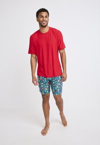 Czerwona koszula z krótkim rękawem w połączeniu z błękitnymi szortami kąpielowymi w kwiecisty wzór. Koszula jest gładka, natomiast szorty mają żywy motyw kwiatowy.