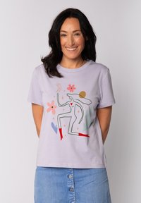 Lavendelkleurig T-shirt van katoen, met een kleurrijk, abstract ontwerp met bloemen, een figuur en rode accenten. Korte mouwen en een ronde hals.