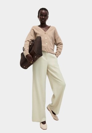 Cárdigan de lana beige con botones dorados, pantalones de pierna ancha verde claro y un bolso de cuero marrón. Unos zapatos planos en tonos neutros completan el look.