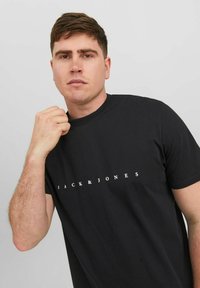 Zwarte katoenen t-shirt met een ronde hals en korte mouwen, met "JACK & JONES" in witte letters over de borst gedrukt. Glad materiaal.