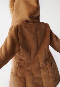 Brun faux pelsjakke med hætte, der har en blød tekstur, lodrette syninger og sidelommer. Stoffet har et blødt og varmt udseende.