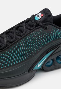 Chaussure Nike Air Max noire avec motif à pois turquoise, lacets noirs et amorti d'air visible dans la semelle près du talon.