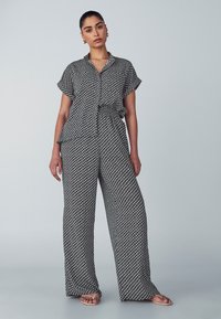 Completo in due pezzi con un motivo geometrico in bianco e nero; maniche corte, vestibilità comoda e cintura in vita, abbinato a pantaloni a gamba larga.