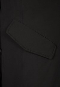 Černá tkanina s hladkým povrchem disponuje výraznou kapsou na rukávu, která ukazuje čistý, moderní design a precizní šití.