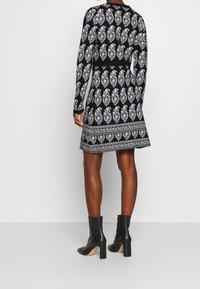 Robe noire avec motifs floraux blancs, manches longues, taille cintrée, jupe évasée et ourlet contrastant. Accompagnée de bottines noires.