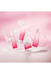 Fyra hudvårdsprodukter visade mot en rosa bakgrund. Flaskorna har en rosa till klar gradient, med runda former och eleganta silverdetaljer.