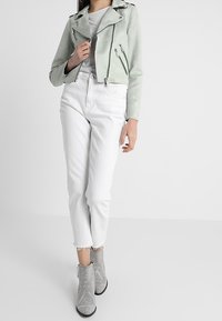 Mintgrön mockajacka i bikerstil med silverfärgade dragkedjor, matchat med vita cropped jeans och grå ankelboots med nitar.