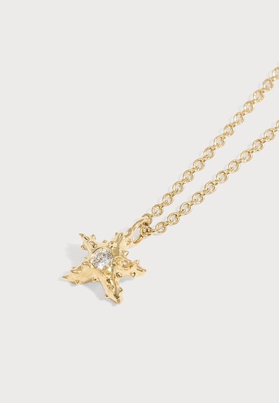 Pendentif en forme d’étoile dorée avec des pointes texturées et une pierre claire centrale sur une fine chaîne en or, fond blanc.