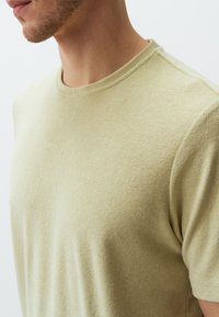 Jasnozielona koszulka z krótkim rękawem wykonana z miękkiej tkaniny. Ma okrągły dekolt i gładką strukturę z subtelnymi detalami szycia.