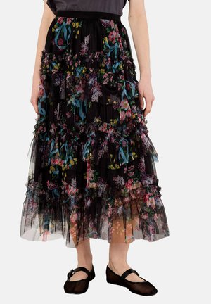 Schwarzer Tüllrock mit geschichteten Rüschen, der ein buntes Blumenmuster aufweist und einen breiten Bund hat. Kombiniert mit einfachen schwarzen Ballerinas.