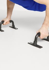 Maniglie push-up in plastica nera con base piatta, dotate di un design curvo per la presa e un piccolo logo Nike su ogni base, poggiate su una superficie chiara.