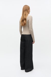 Bēšs ribots garroku tops kopā ar vaļīgiem melniem džinsa džinsiem. Apģērbs ir vienkārša, pieguloša dizaina ar vieglām šūšanas detaļām.