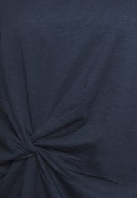 Tmavě modrá tkanina se zkrouceným detailem uprostřed, ukazující jemnou strukturu a neformální styl, vhodná pro uvolněné outfity.