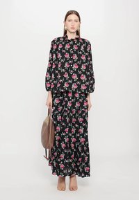 Blomster på svart bakgrunn, langermet bluse med rund hals, matchende lang skjørt, lett stoff, parret med en beige veske.
