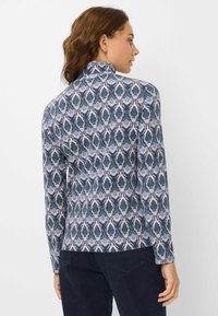 Maglia a maniche lunghe con un motivo a rombi blu e verdi su sfondo scuro, con colletto alto e una texture di tessuto liscia.