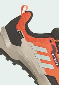 Orange och svart vandringsko med meshöverdel, Gore-Tex-label, tre reflekterande ränder, texturerad mellansula och robust ytsula.