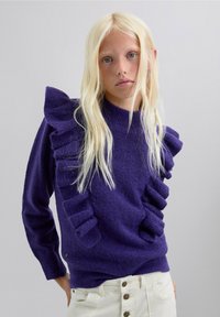 Suéter morado con acentos con volantes a lo largo de un lado, material de punto texturizado, cuello redondo, puños ajustados, combinado con pantalones color crema.