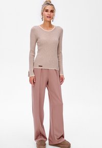 Beige ribgebreid trui met een witte kraag, gecombineerd met zachtroze brede broekspijpen. Opvallende details zijn de zijsplitten en een klein bruin label.