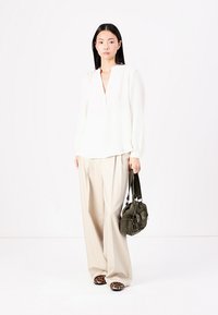 Hvit langermet bluse med V-hals, kombinert med beige vide bukser. Accessorert med en grønn veske og dyreprint leiligheter.