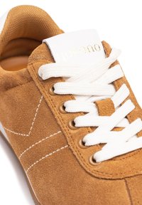 Brown suede sneaker with white laces, gold eyelets, and white tongue featuring embossed logo. Side stitching creates a sleek design.