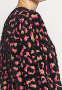Fluffig svart tröja med leopardmönster i rosa och beige. Har en texturerad stickning som framhäver framträdande mönster och färger.