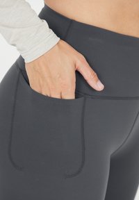 Grijze high-waisted leggings met een zijzak, met een gladde textuur en versterkte stiksels, gecombineerd met een licht lange mouwen top.