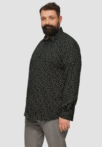 Zwarte longsleeve shirt met witte cirkelvormige patronen, met kraagontwerp en knoopsluiting aan de voorkant, gecombineerd met lichtgrijze broeken.