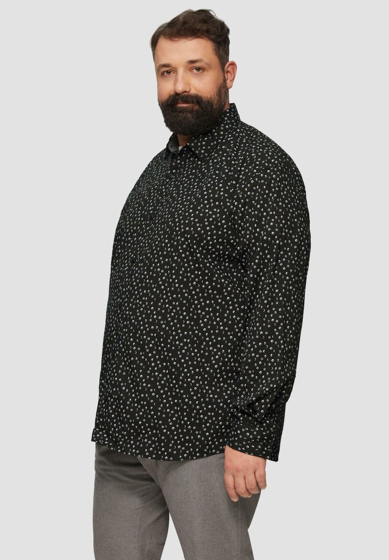 Zwarte longsleeve shirt met witte cirkelvormige patronen, met kraagontwerp en knoopsluiting aan de voorkant, gecombineerd met lichtgrijze broeken.
