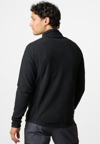 Schwarzer Fleece-Pullover mit hohem Kragen, Seitennähten und langen Ärmeln. Glatte Textur mit dehnbarem Stoff, geeignet zum Lagenlook.