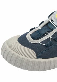 Gros plan sur la pointe d'une basket bleu marine et grise avec une semelle en caoutchouc texturée, une tige en tissu et un système de laçage élastique blanc sécurisé.