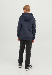 Felpa blu navy con cappuccio, polsini e orlo a coste. Indossata con jeans neri e sneakers nere con dettagli bianchi.
