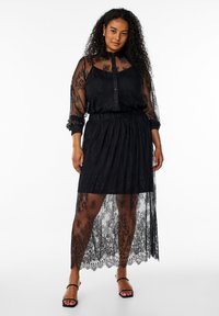 Abito in pizzo nero con parte superiore a camicia con bottoni e gonna trasparente, dotato di una vita elastica e motivi floreali in tutto l'abito.