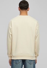 Cream fleece sweatshirt with a crew neckline, drop shoulders, ribbed cuffs, and hem. Asymmetrical stitching detail on the back.