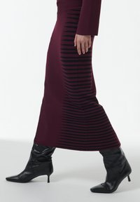 Falda de punto burdeos con rayas negras horizontales. Silueta ajustada hasta el tobillo con cintura acanalada. Botas negras hasta el tobillo.