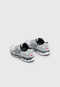 Ett par vita och grå ASICS GEL löparskor med svart inredning, visade på en enkel vit bakgrund.